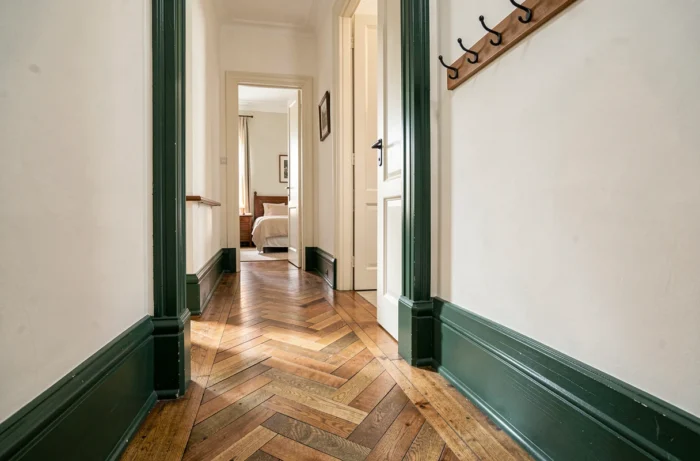 Couloir d'appartement classique avec plinthes et encadrements de portes repeints en vert forêt profond contrastant avec les murs blanc cassé
